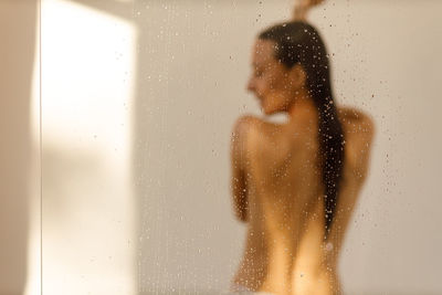 Shirtless young woman standing against wall