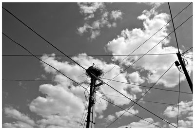 Low angle view of stork on nest over power line against sky