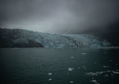 Scenic view of sea by mountain against sky