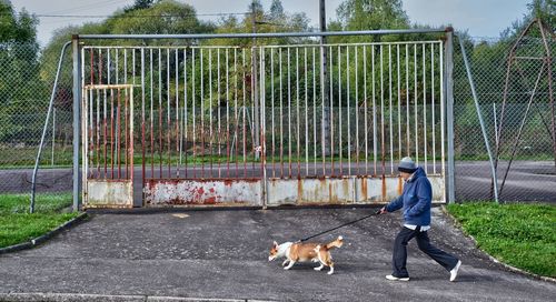 Full length of man with dog walking on road by abandoned gate