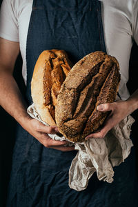 Crop unrecognizable male baker in apron demonstrating loaf of fresh crispy breads in kitchen