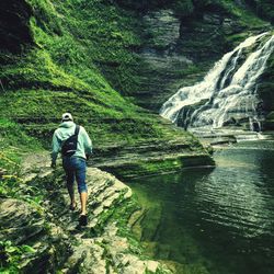 Rear view full length of man walking on rocks against waterfall