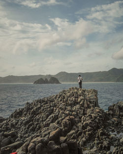 Man standing on rock by sea against sky
