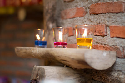 Colorful burning tea light candles on shelf by brick wall