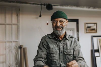 Portrait of cheerful male owner wearing knit hat and eyeglasses in workshop