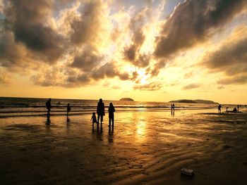 Silhouette people on beach against sky during sunset