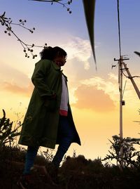 Low angle view of woman standing on land against sky during sunset