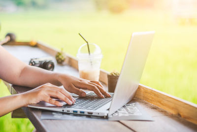 Cropped hands of woman using laptop at cafe