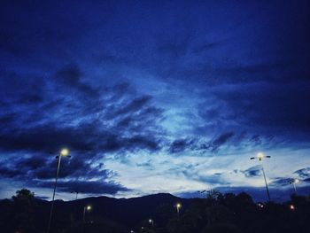 Low angle view of illuminated street light against cloudy sky