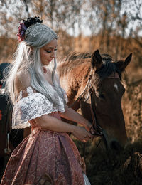 Smiling young woman wearing costume touching horse outdoors