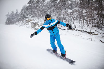 Man snowboarding by trees on snow covered mountain