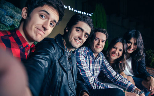 Portrait of friends smiling while sitting at patio during night