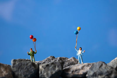 Low angle view of people on rock against blue sky