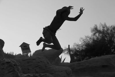 Low angle view of boy in mid-air by rock formations against sky
