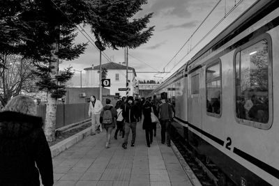 People at railroad station in city against sky