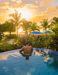 Rear view of woman sitting on beach against sky during sunset