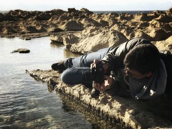 Man lying on rock while photographing water