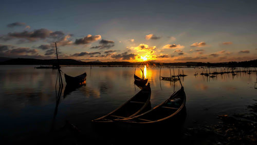 Sailboats moored in lake against sky during sunset