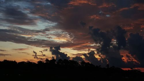 Silhouette trees against dramatic sky during sunset