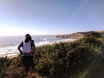 Rear view of father piggybacking daughter while looking at sea