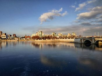 Bridge over river by buildings against sky in city