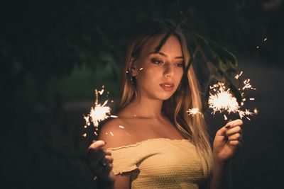 Young woman holding lit sparkler at night