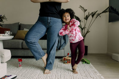 Mother and daughter doing tree pose while practicing yoga in living room