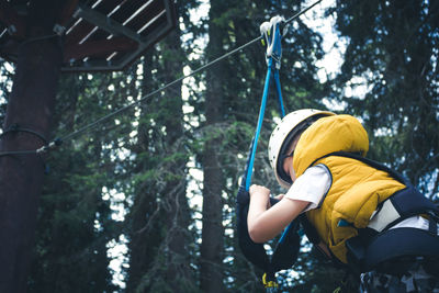 Below view of small boy on canopy tour in the forest.