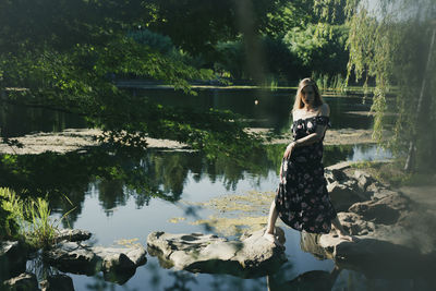 Full length of woman standing by lake against trees