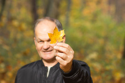 Happy senior man holding in his hand yellow maple leaf in the autumn city park. active seniors.