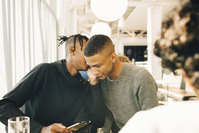 Teenage boy whispering into male friend's ear in restaurant
