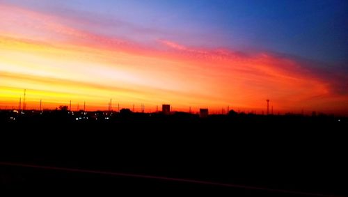 Silhouette city against dramatic sky during sunset