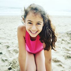 Close-up portrait of cheerful girl kneeling at beach