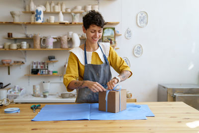 Female seller in craft crockery and handcraft pottery shop pack and decorate gift box for customer