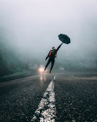 Man with umbrella levitating over wet street during rainy season