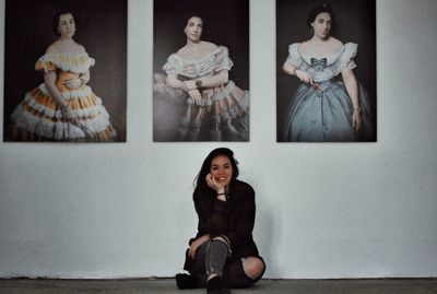 Portrait of a smiling young woman sitting against wall