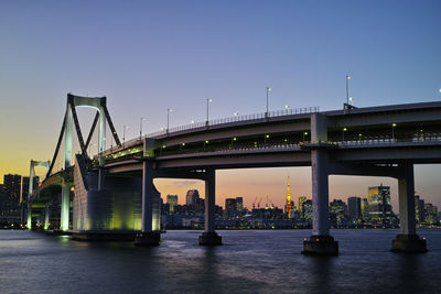 Rainbow bridge over river against clear sky at dusk