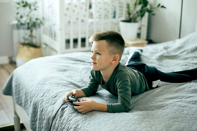 Cute boy playing video game while lying on bed at home