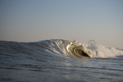 Waves splashing in sea against clear sky during sunset