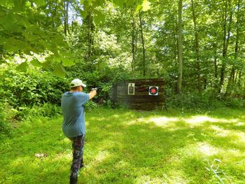 Rear view of man practicing target shooting in forest