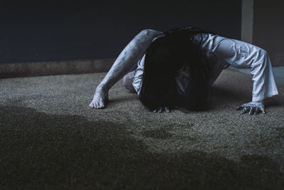 Spooky young woman crouching on floor against wall