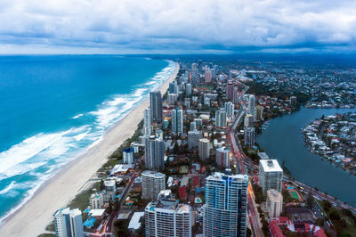 Aerial view of cityscape by sea against cloudy sky