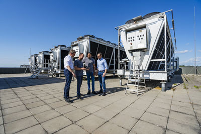 Businessmen and employees having a meeting on rooftop beside refrigeration installation