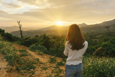 Rear view of woman on landscape against sunset