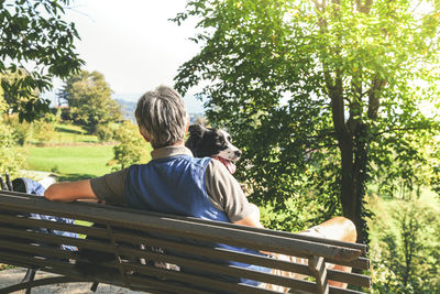 Man and his dog sitting on a park bench looking the mountain panorama. friends together at the park