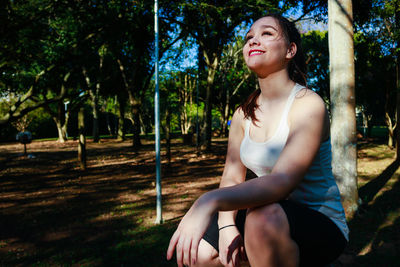 Beautiful woman smiling while crouching against tree at park