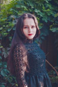 Portrait of young woman with long brown hair standing by plants