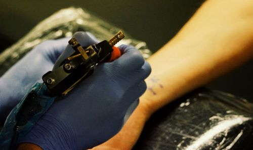 Cropped hand of person tattooing on woman hand