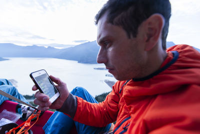 Perplex man looking at phone sitting on portaledge at sunset thinking