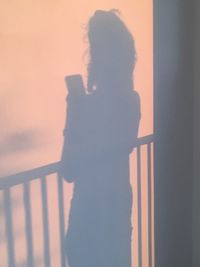 Silhouette woman standing against wall during sunset